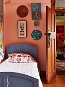 Wooden bed painted purple against pink wall with framed collection of butterflies and pictures next to open wooden door