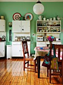 Holzstühle um Tisch auf gepflegtem Dielenboden in schlichter, funktionaler Küche, weiße Schränke an grün getönter Wand