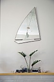 Mirror in shape of sailing boat above arrangement on mantelpiece