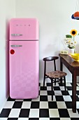 Pink, 50s-style fridge-freezer next to dining area on chequered floor