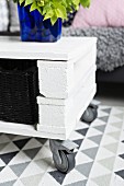 Simple, DIY coffee table on castors made from white-painted wooden blocks and boards with black-painted basket and deep blue glass vase