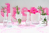Sprigs of rosemary in small glass vessels dipped in white paint; pink string art picture in background