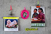Pictures of babies and children stuck on concrete wall as mood board - clips and clothes hanger with neon-coloured strips, crocheted frame around nostalgic picture of child