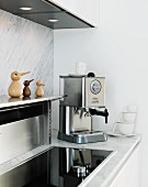 White kitchen with marble back wall and worksurface, stainless steel shelf, integrated hob and espresso machine