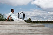 Junger Mann sitzt auf einem Holzsteg am See