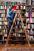 A man reading on a ladder in a home library