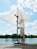 A young man opening a patio parasol on a jetty