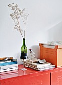 Vase made from wine glass and cut-off wine bottle, stack of books and files on red metal cabinet