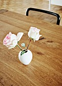 Two roses in small, white retro vase on wooden table