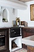 Old masonry kitchen cooker with firewood store integrated into kitchen counter below arched niche in wall