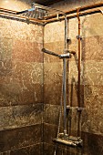 Modern shower head, tap fittings and exposed copper piping on brown marbled wall tiles