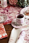 Crockery and table linen with red toile de jouy patterns on rustic wooden table