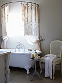 Weisser Stuhl und Beistelltisch neben Vintage Badewanne, oberhalb halbkreisförmige Vorhangstange mit Duschvorhang