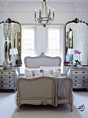 French-style bedroom - bed with curved wooden frame below window flanked by mirrors and glass pendants hanging from ceiling