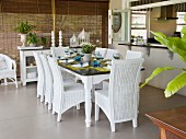 White wicker chairs around set table in loggia in front of closed bamboo blinds