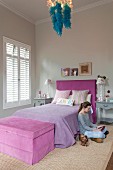 Teenager's bedroom in shades of lilac with blue feather boa draped on chandelier; girl and dog sitting on floor