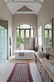 Gräumiges Badezimmer mit freistehender Badewanne und Paravent vor Balkontür