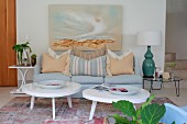 Two coffee tables with white, amorphous tops and pale blue sofa below landscape on wall