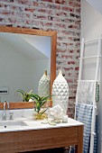 Simple wooden washstand with white stone counter and framed mirror on exposed brick wall; white ladder used as towel rack