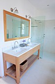 Washstand with twin undermount basins, framed mirror on wall and floor-level shower area with glass partition in modern bathroom
