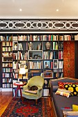 Antique, green armchair and Biedermeier-style sofa in front of modern bookcase below black and white stencilled frieze on wall