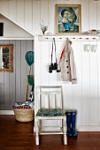 Kitchen chair below portrait and coat pegs on white, wood-panelled wall in foyer