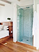 Shower with mosaic tiles and glass partition integrated into simple bedroom with parquet floor
