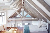 Guest bed on mezzanine below pale roof beams in modern holiday home