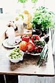 Dishes of fruit and vegetables and pots of herbs on rustic wooden table