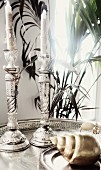Two ornate silver candlesticks on tray behind snail shell ornament