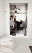 Stack of cushions on white floor in front of doorway leading to kitchen; woman standing at dining table