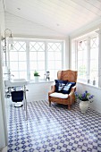 Sink and wicker armchair in conservatory-style extension with blue and white floor tiles and maritime scatter cushions