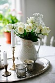 White roses and gypsophila in china vase next to candlesticks & tealight holders on silver tray; vintage arrangement