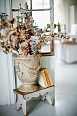 Branches of fabric leaves in vase in antique Greek style in front of lattice partition