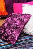 Cushion with silk-effect, purple cover and pattern of roses on rag rug