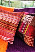 Colourful scatter cushions in various shades of red with Oriental-style striped and patchwork covers on couch