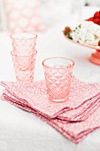 Rosafarbige Reto-Trinkgläser auf rosaweiß gemusterten Stoffservietten mit Vintageflair