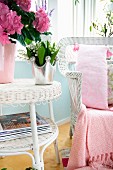 Vase of flowers on white wicker side table next to matching armchair with pink patterned cushions