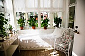 White rattan armchair and couch with lace blanket below window and potted plants on windowsills in loggia