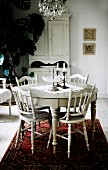 Round dining table and chairs with turned legs painted white on red Oriental rug in rustic interior