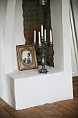 White candles in five-armed candelabra and vintage photo on masonry plinth