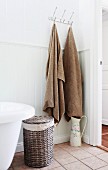 Bath towels hanging from hooks, old water jug with floral motif and laundry basket in country-house bathroom