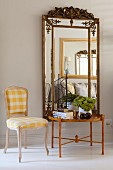 Rococo chair with white and yellow gingham upholstery next to side table below mirror with ornate frame