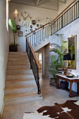 Staircase in open-plan foyer with animal-skin rug, antique console table and potted palms