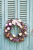 Wreath decorated with flowers and baubles hung on turquoise wooden door
