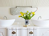Vintage chest of drawers converted into washstand with twin countertop basins; vase of yellow tulips