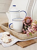 Rustic mug and coffee pot next to protea flowers on wicker tray