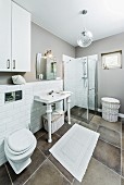 Bad in Weiß und Grau - Waschtisch mit weissen, gedrechselten Beinen vor halbhoch gefliester Wand und bodenebene Duschkabine aus Glas