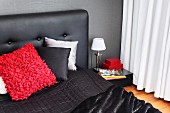Scatter cushions on black bed with upholstered headboard against dark wall