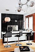 A black and white designer kitchen with shiny cupboards, leather stools at the breakfast bar and various round lamps